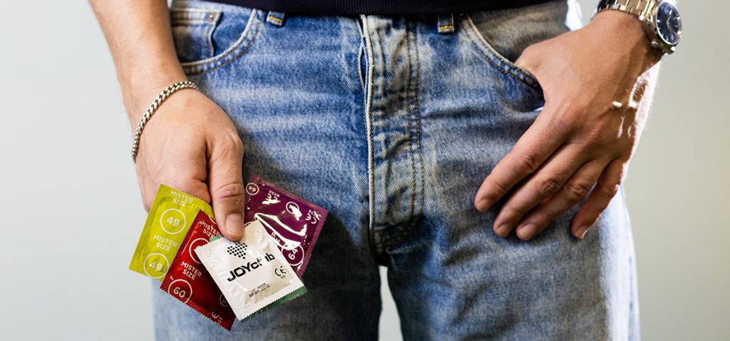 Mann hält Kondome in verschiedenen Größen in der Hand. 